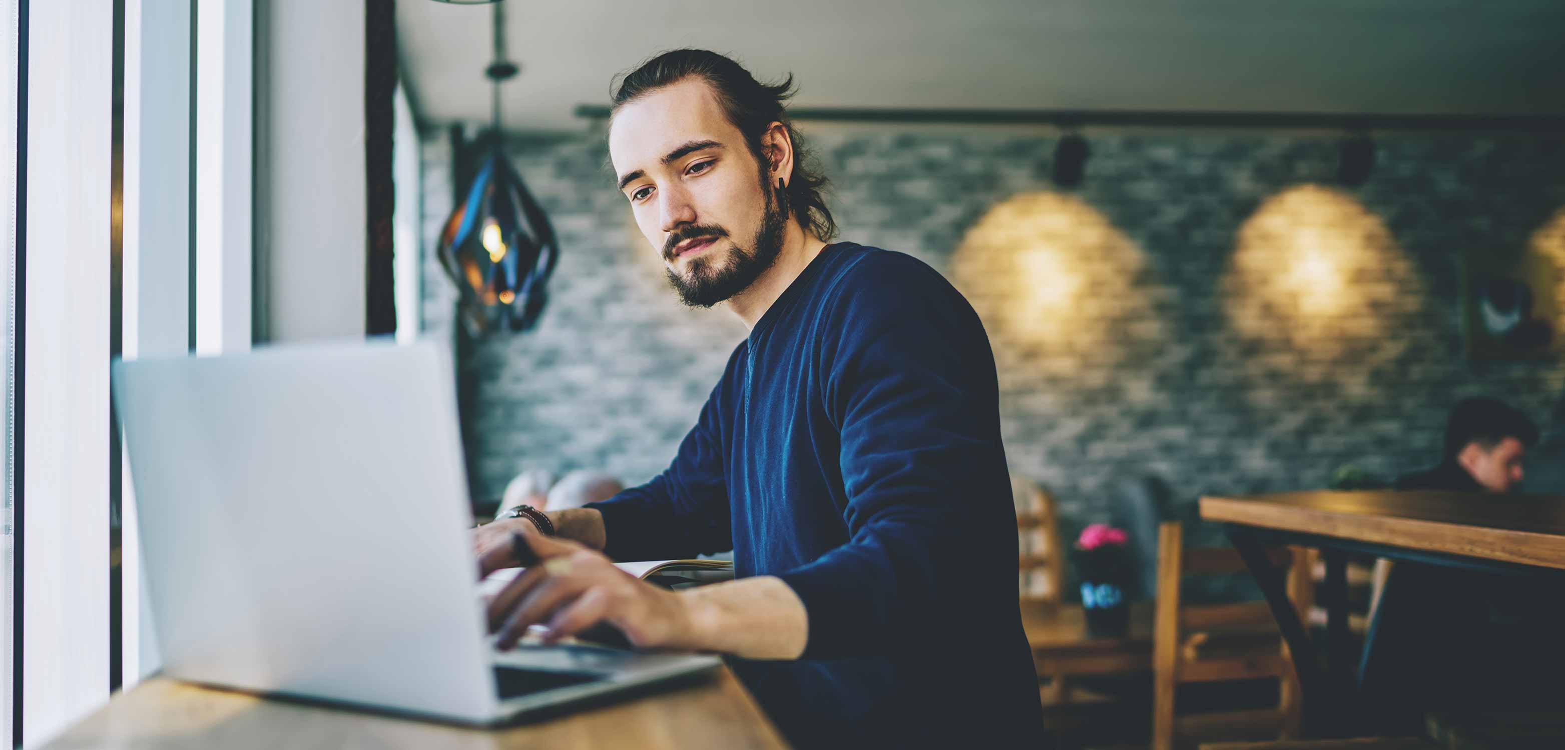 Junger Mann sitzt in einem Kaffeehaus liest die News des Digital Makers Hub